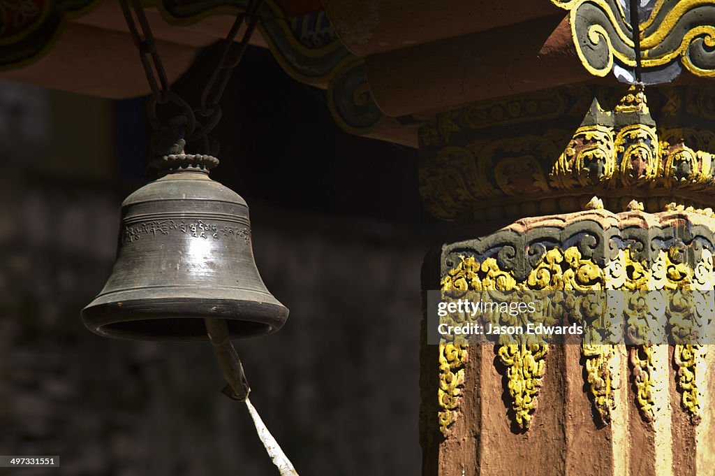 A brass meditation bell hangs from an ornate eve in a Buddhist monastery.