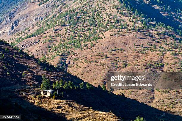 a traditional bhutanese farmhouse on a rugged mountainside catches the last rays of the setting sun. - baron photos et images de collection