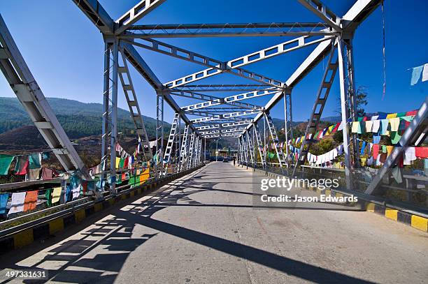 prayer flags hanging from the steel girders of a bridge crossing the paro river. - east bhutan stock pictures, royalty-free photos & images