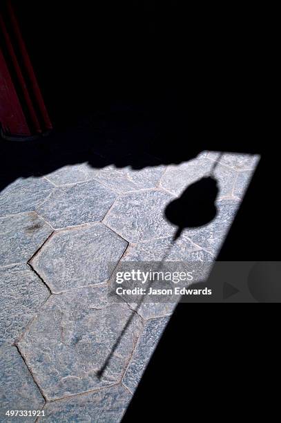 the shadow of a brass bell and chain hanging in a doorway to a buddhist monastery. - hand bell stock pictures, royalty-free photos & images