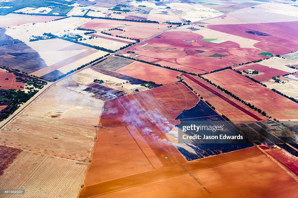 Smoke rises from agricultural crops being burned on a vast plain of arid farmland.