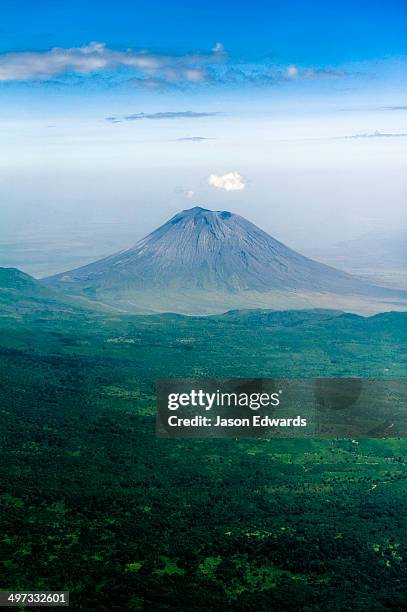 clouds circle the summit of primeval volcano caldera shrouded in forests above the savannah plain. - tansania stock-fotos und bilder