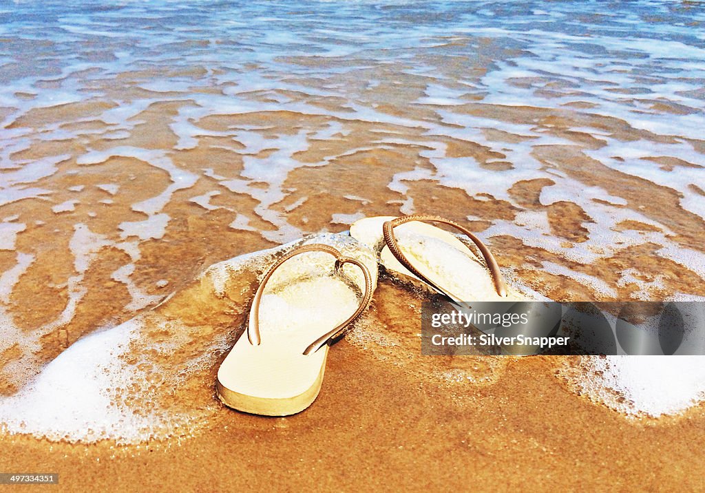 Flip flops on beach in surf