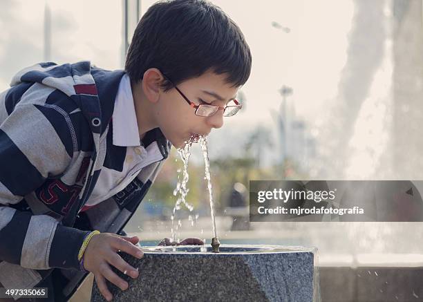 spain, cordoba, boy (12-13) drinking water from fountain in park - drinkwaterfontein stockfoto's en -beelden