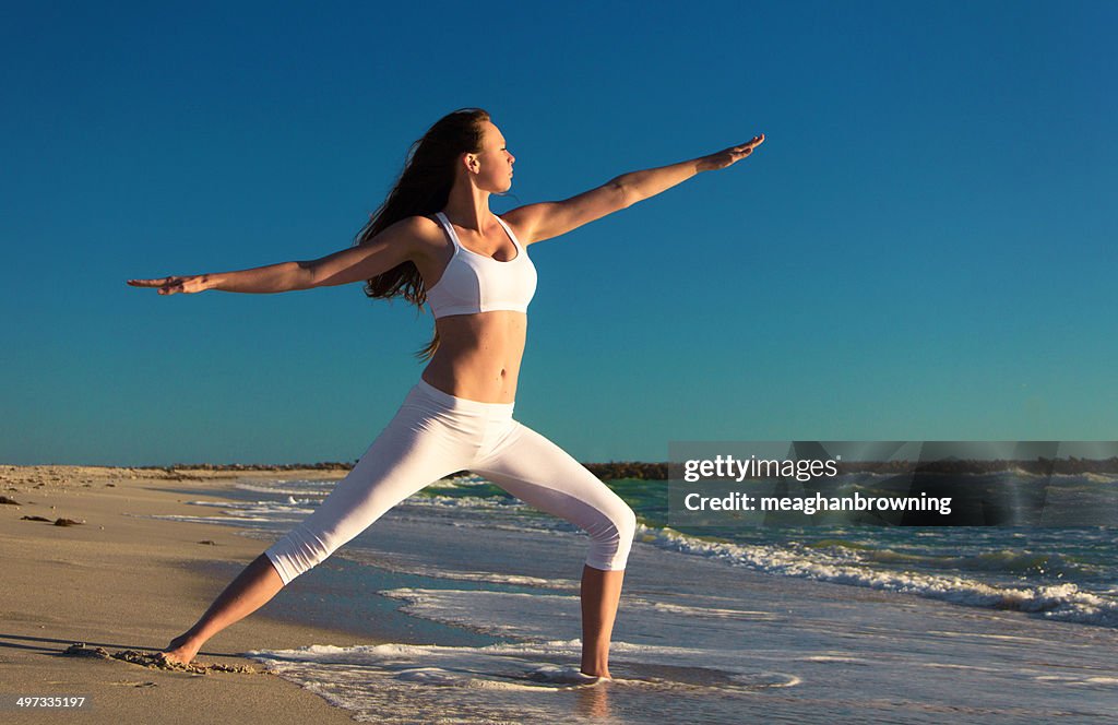 Woman practicing warrior 2 yoga pose on beach