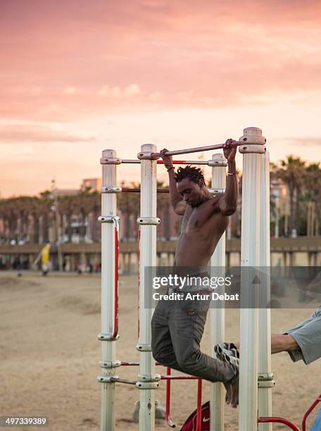 Guy doing bar pull ups on Crossfit routine in a open outside gym in the shoreline at sunset.