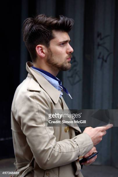 Well-dressed dark haired young man with a beard wearing a trench coat and holding a smartphone, London, England