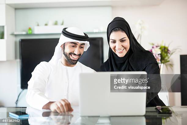 content middle eastern couple viewing photos and videos on laptop - emirati couple stock pictures, royalty-free photos & images