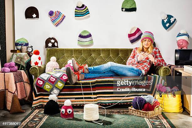 bild einer strickenden, jungen frau auf einer couch mit wintermützen - blonde long legs stock-fotos und bilder