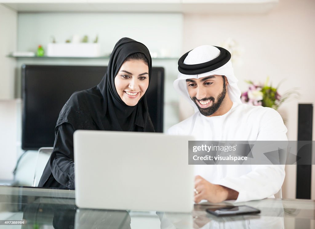 Emirati marido y mujer usando una computadora portátil en su hogar