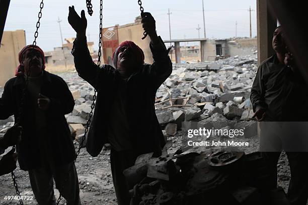 Yazidis work to lift an engine to salvage it from the rubble of an auto repair shop destroyed by an airstrike on November 16, 2015 in Sinjar, Iraq....