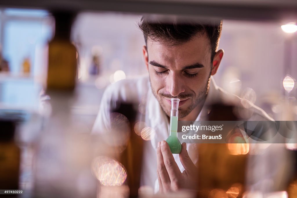 Smiling chemist smelling substances from a beaker in a laboratory.