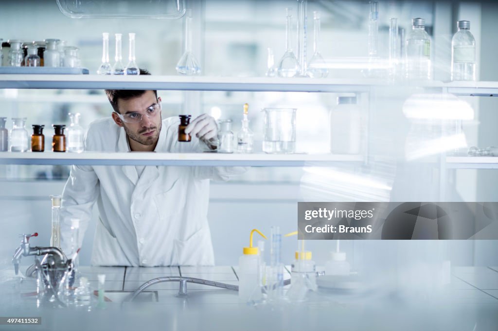 Young chemist choosing the right bottle in a laboratory.