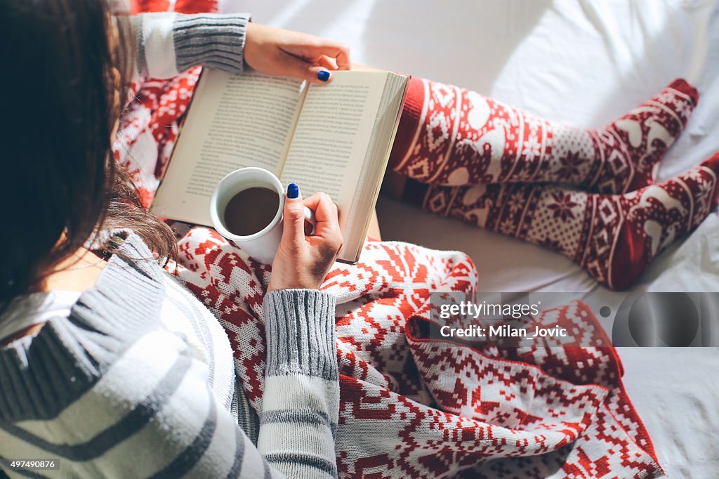 Girl in bed with coffee cup reading a book