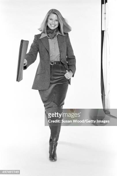 American model Christie Brinkley poses, dressed in business attire, against a white background, 1976. She wears a neckerchief, a tweed jacket over a...