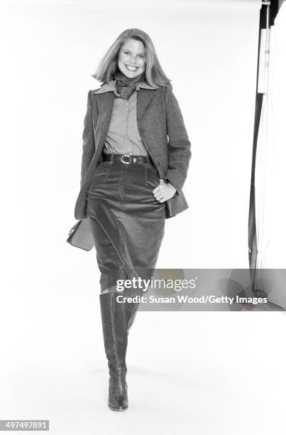 American model Christie Brinkley poses, dressed in business attire, against a white background, 1976. She wears a neckerchief, a tweed jacket over a...