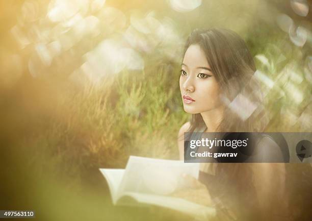 asian girl with book shot through objects using selective focus. - hand turning page stock pictures, royalty-free photos & images