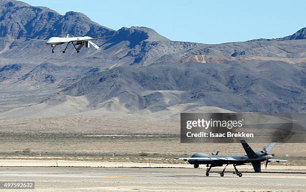 An MQ-1B Predator remotely piloted aircraft flies past a MQ-9 Reaper RPA as it taxis during a training mission at Creech Air Force Base on November...