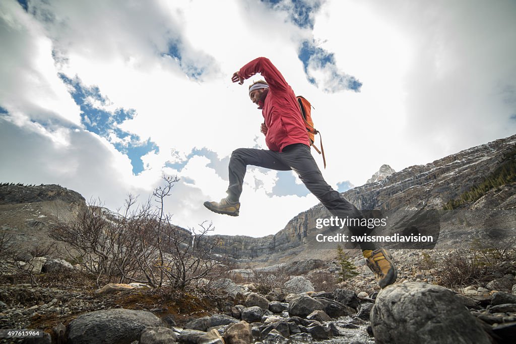 Hiker jumping over mountain river