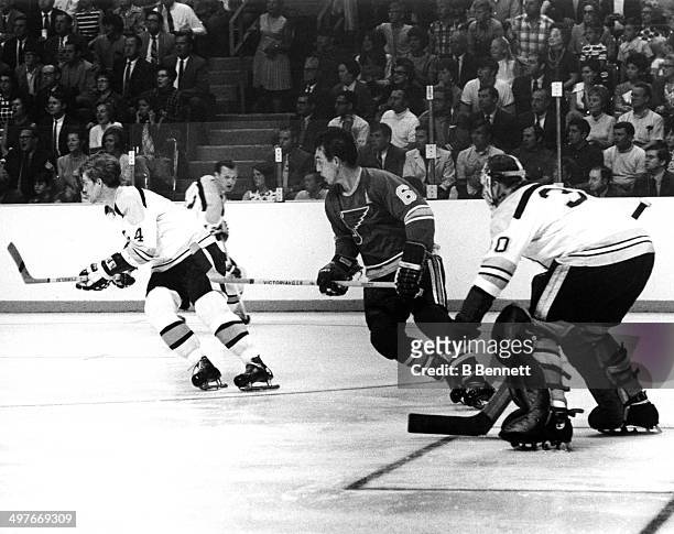 Bobby Orr of the Boston Bruins skates on the ice as he is followed by Jim Roberts of the St. Louis Blues as goalie Gerry Cheevers looks on during...