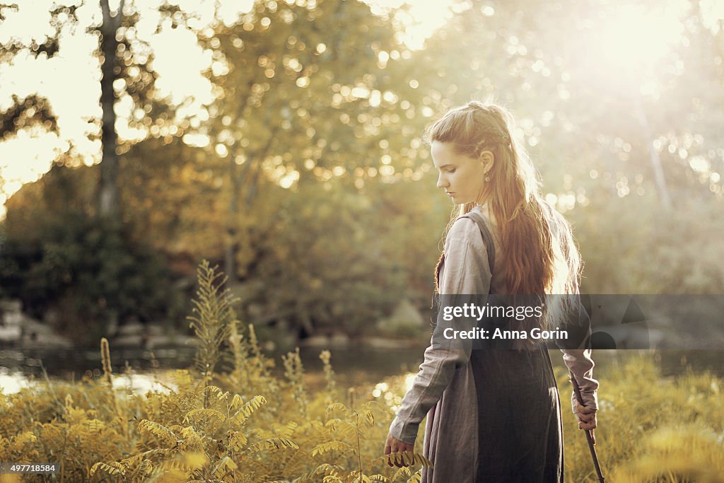 Young woman with long hair in period viking costume looks down, turning, outdoors and sunlit