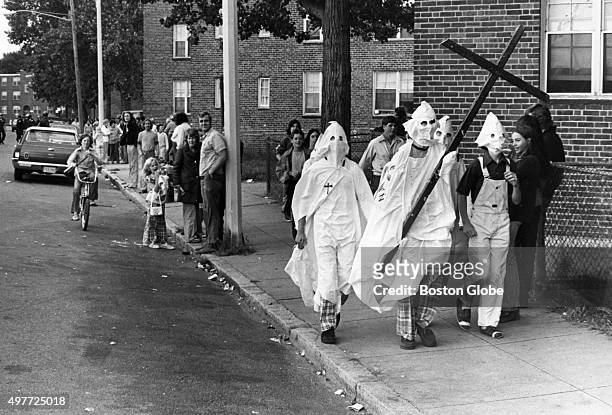 Group of Ku Klux Klan impersonators carry a large cross as they walk past the Old Colony housing project on Columbia Road in Boston on Sept. 18,...