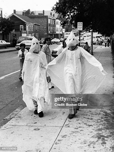 Two teens impersonating Ku Klux Klan members, dressed in white sheets and pointed hoods, walk down Dorchester Street near Old Colony Avenue in Boston...