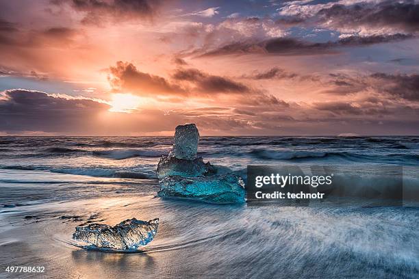 icebergs floating on icy beach at sunrise, south iceland - iceberg ice formation stockfoto's en -beelden