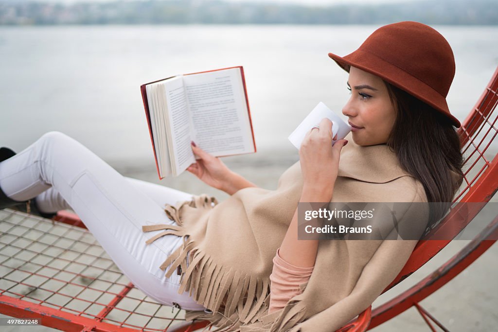 Junge Frau, die in ein Buch und warmen Getränk im Freien.