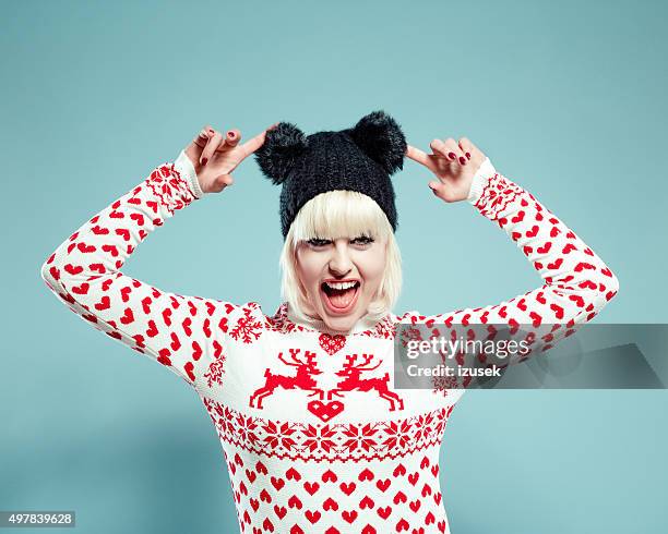 excited blonde young woman wearing xmas sweater and bobble hat - cardigan stock pictures, royalty-free photos & images