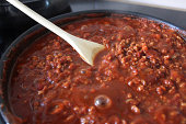 Image of Bolognese sauce cooking in frying pan, wooden spoon