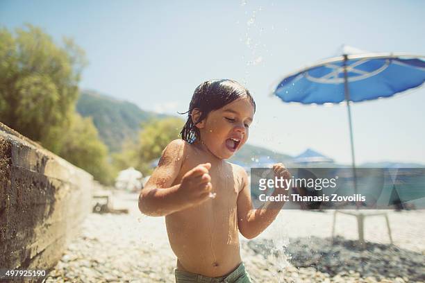 small boy playing with the shower on the beach - greece holiday foto e immagini stock
