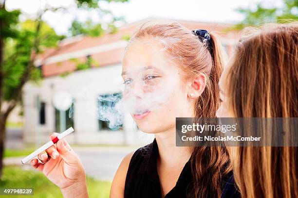 preteen girl tries e-cigarette with her friend - electronic cigarette stockfoto's en -beelden