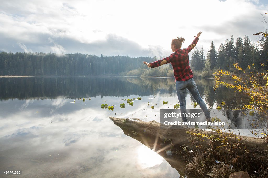 Young woman balances on a tree log above the lake