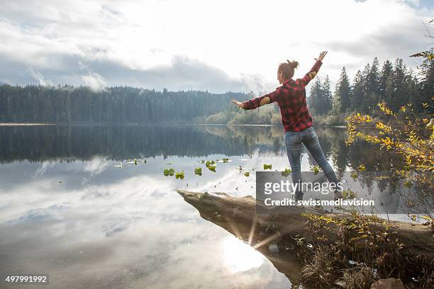 young woman balances on a tree log above the lake - vancouver island stock pictures, royalty-free photos & images