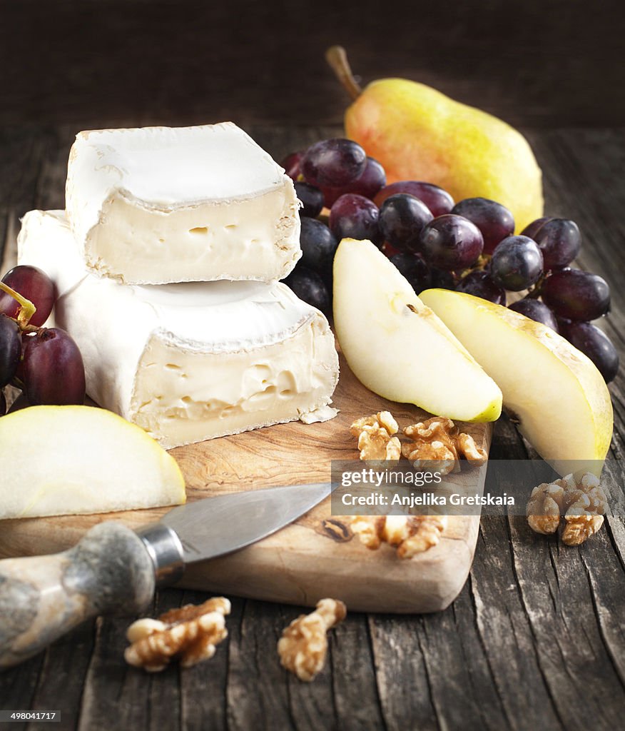 Cheese Brie with pear and grapes on a wooden board