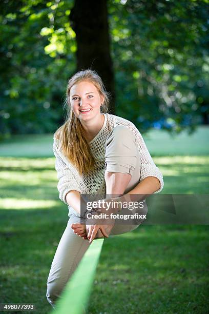 young woman in park sitting on a slackline - slackline stockfoto's en -beelden