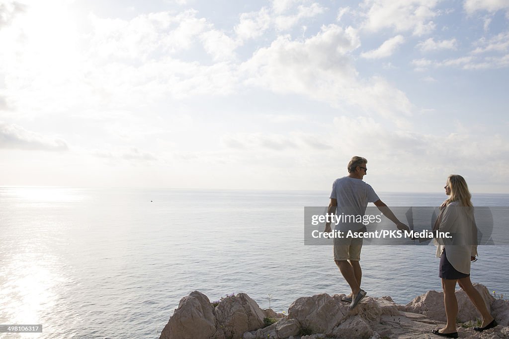 Couple reach to hold hands, sea cliff