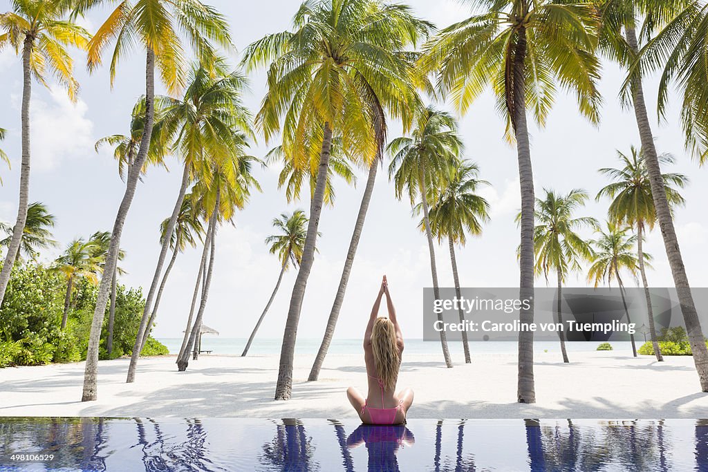 Woman doing yoga by seaside infinity pool