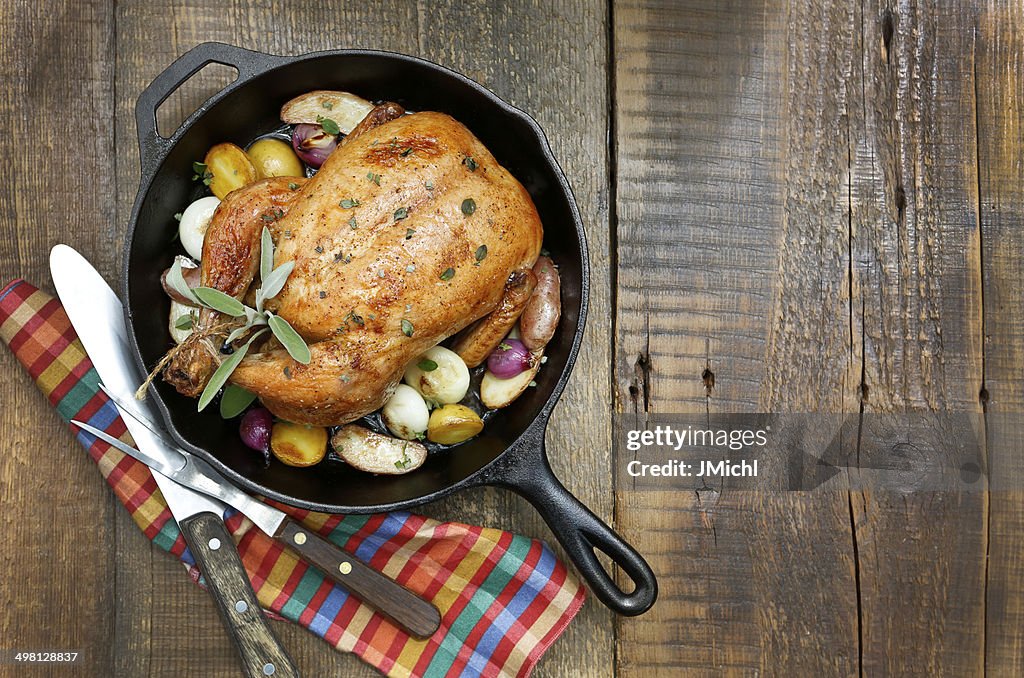 Frango Assado com batatas e cebolas em ferro fundido recipiente.