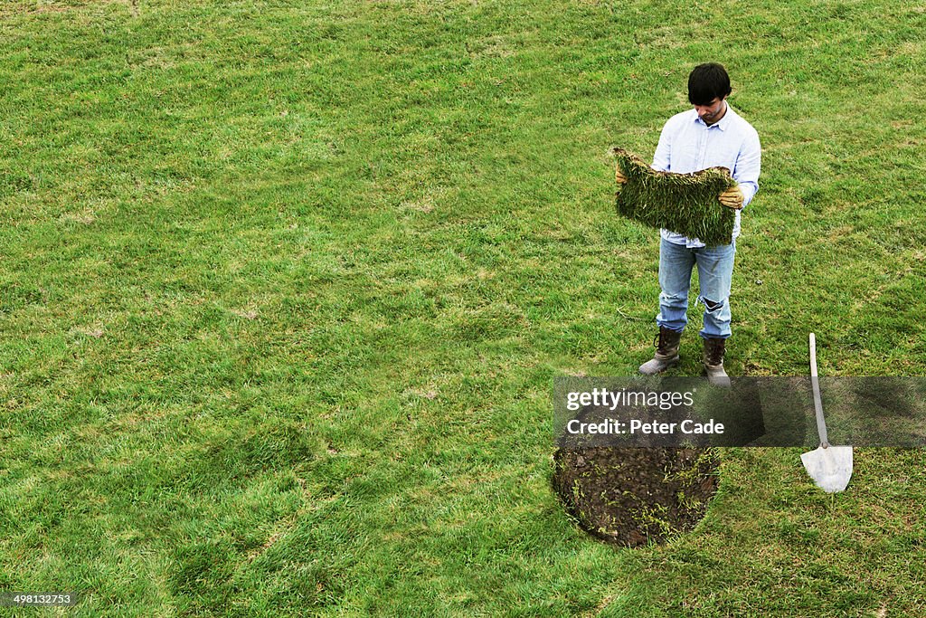 Man with square turf to lay in round gap on lawn