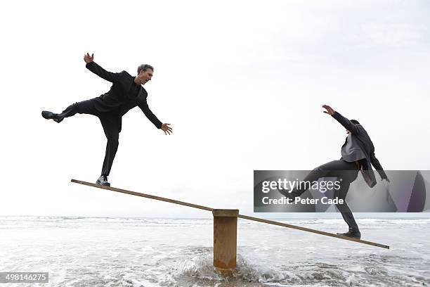 two male executives balancing on seesaw - seesaw foto e immagini stock