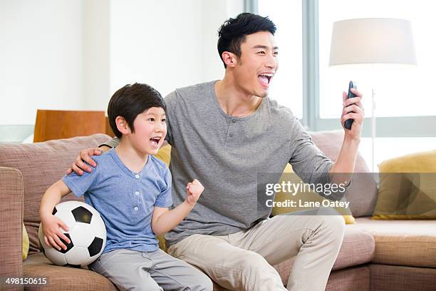 excited father and son watching football on tv - china fans cheer stock pictures, royalty-free photos & images