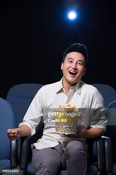 young man watching movie in cinema with popcorn in hand - front row seat stock pictures, royalty-free photos & images