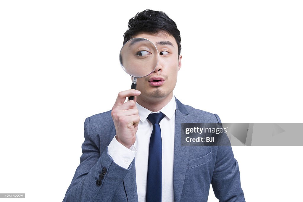 Young businessman looking through magnifying glass