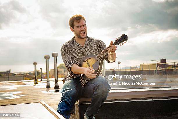 young man rocking his mandolin on brooklyn rooftop - mandolin stock pictures, royalty-free photos & images