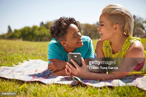 lesbian couple lying on picnic blanket in park - corte de pelo con media cabeza rapada fotografías e imágenes de stock