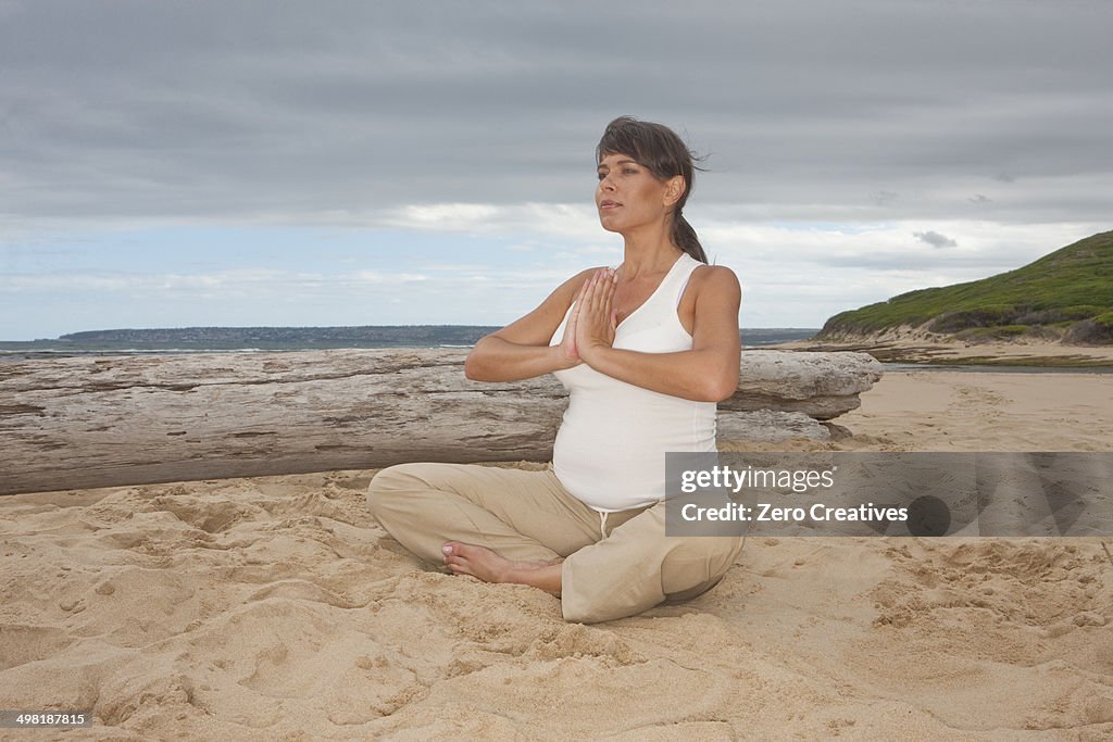 Pregnant mid adult woman practicing yoga on beach