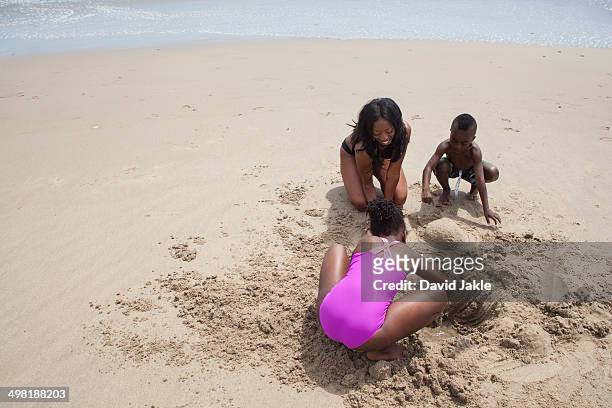 mother and children digging in sand on beach - digging beach photos et images de collection