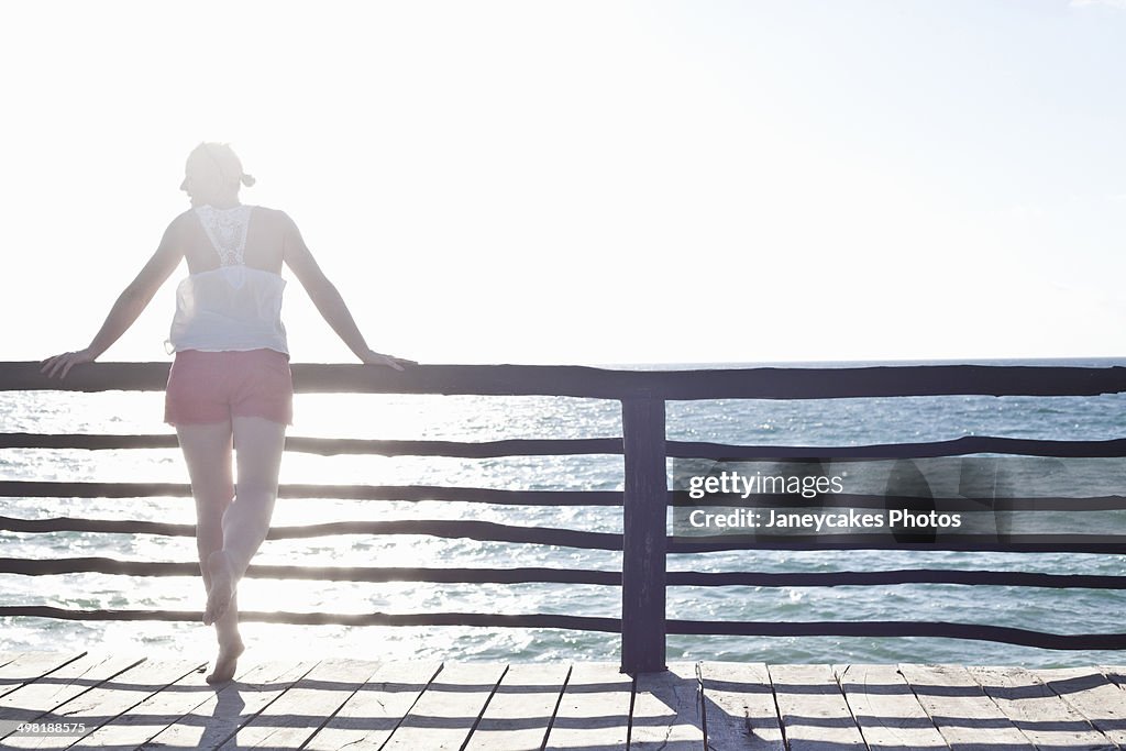 Woman leaning on fence, looking out to sea in Tulum, Mexico